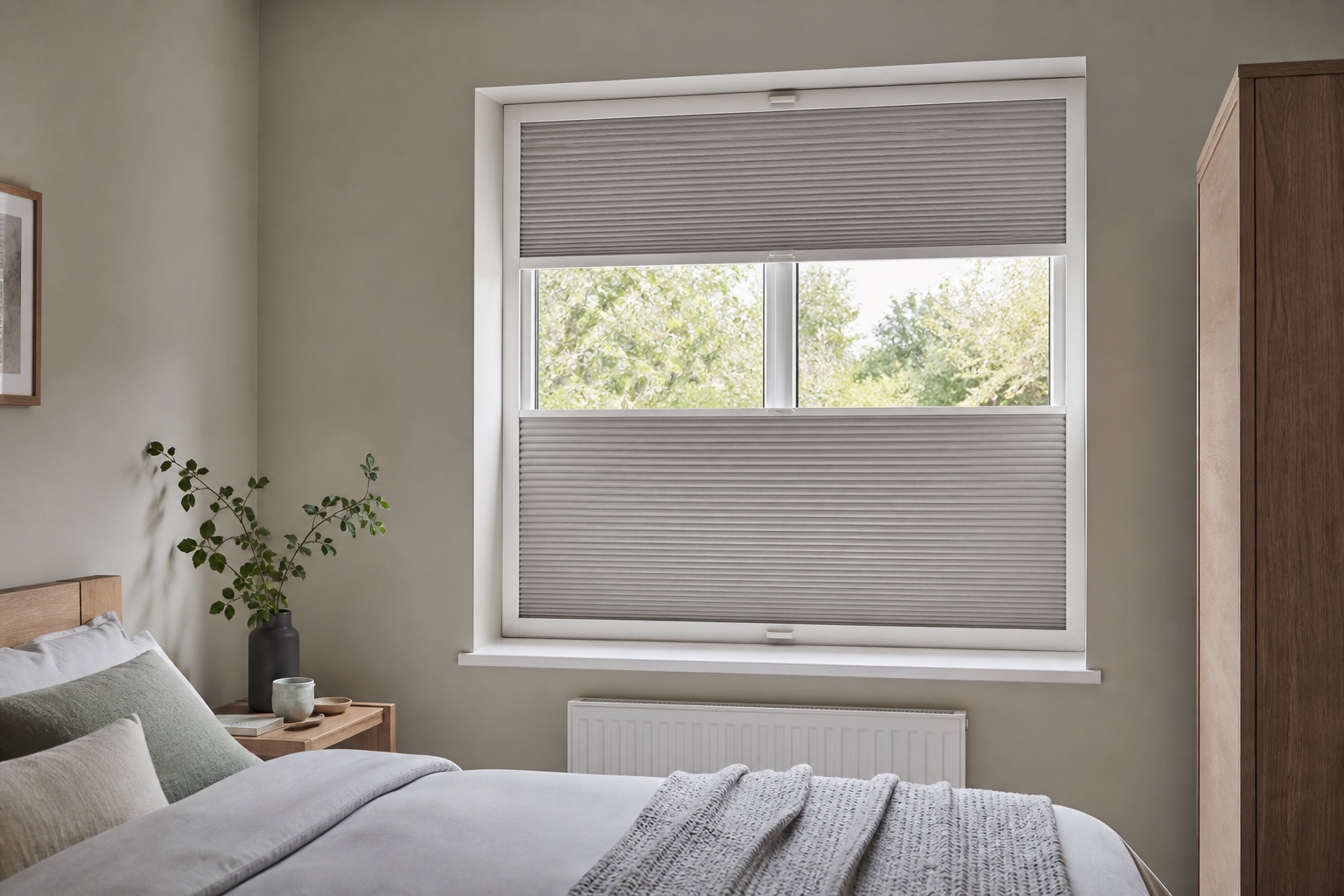 Grey pleated blinds covering the upper and lower parts of a bedroom window